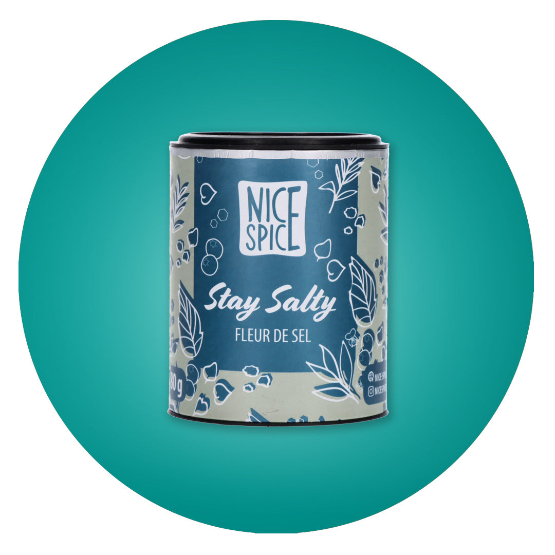 NICE SPICE Stay Salty Fleur de Sel in metallblauer zylinderförmiger Dose in verspieltem Design vor türkisem Hintergrund